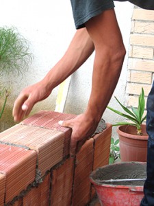 Man's arms laying bricks around a patio